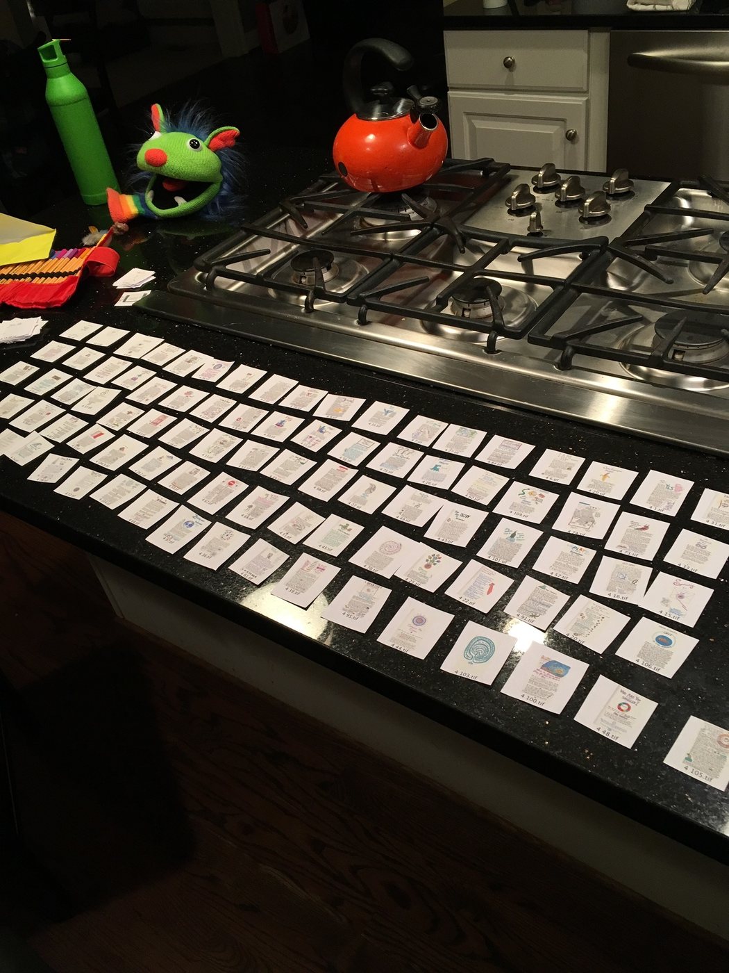 Rows of Cosmic Journal pages laid out across a kitchen island late at night